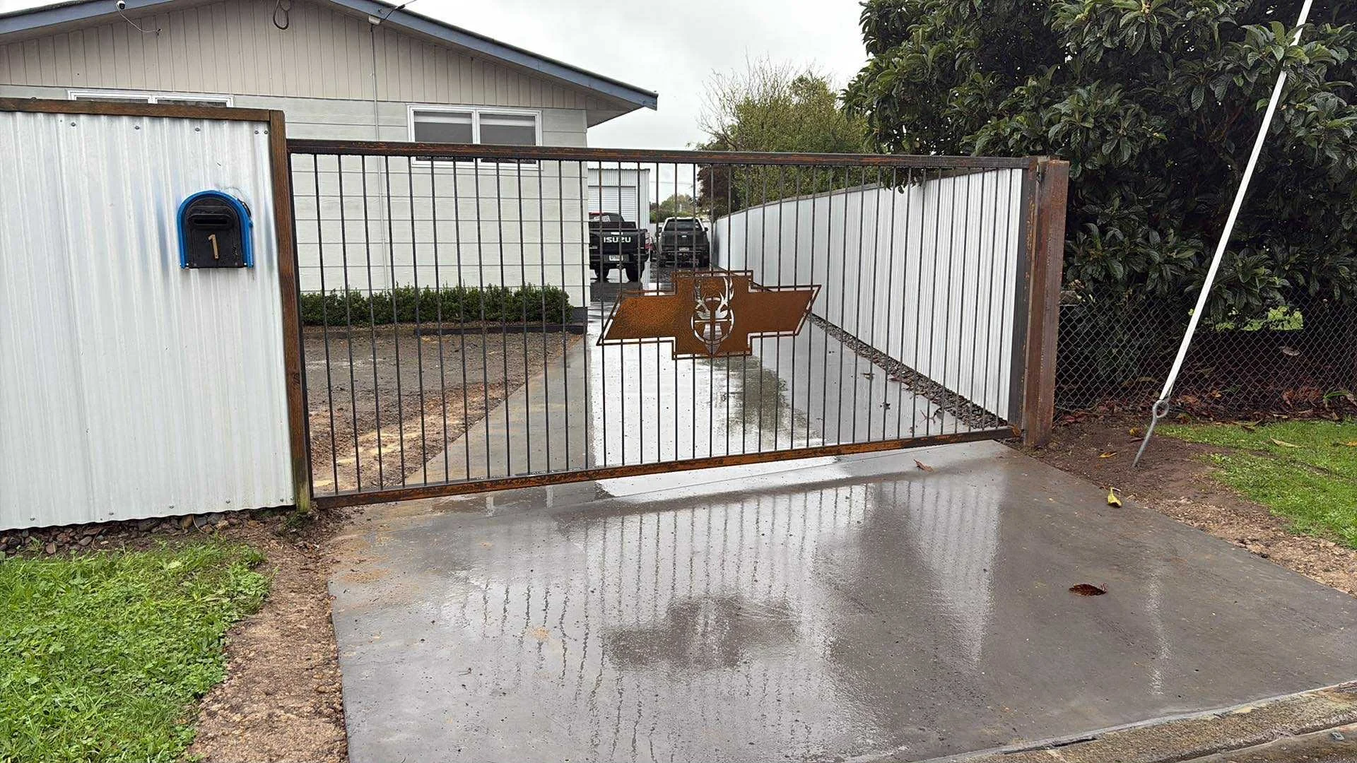 Steel driveway gate with a laser cut emblem in the middle, fitted at a house