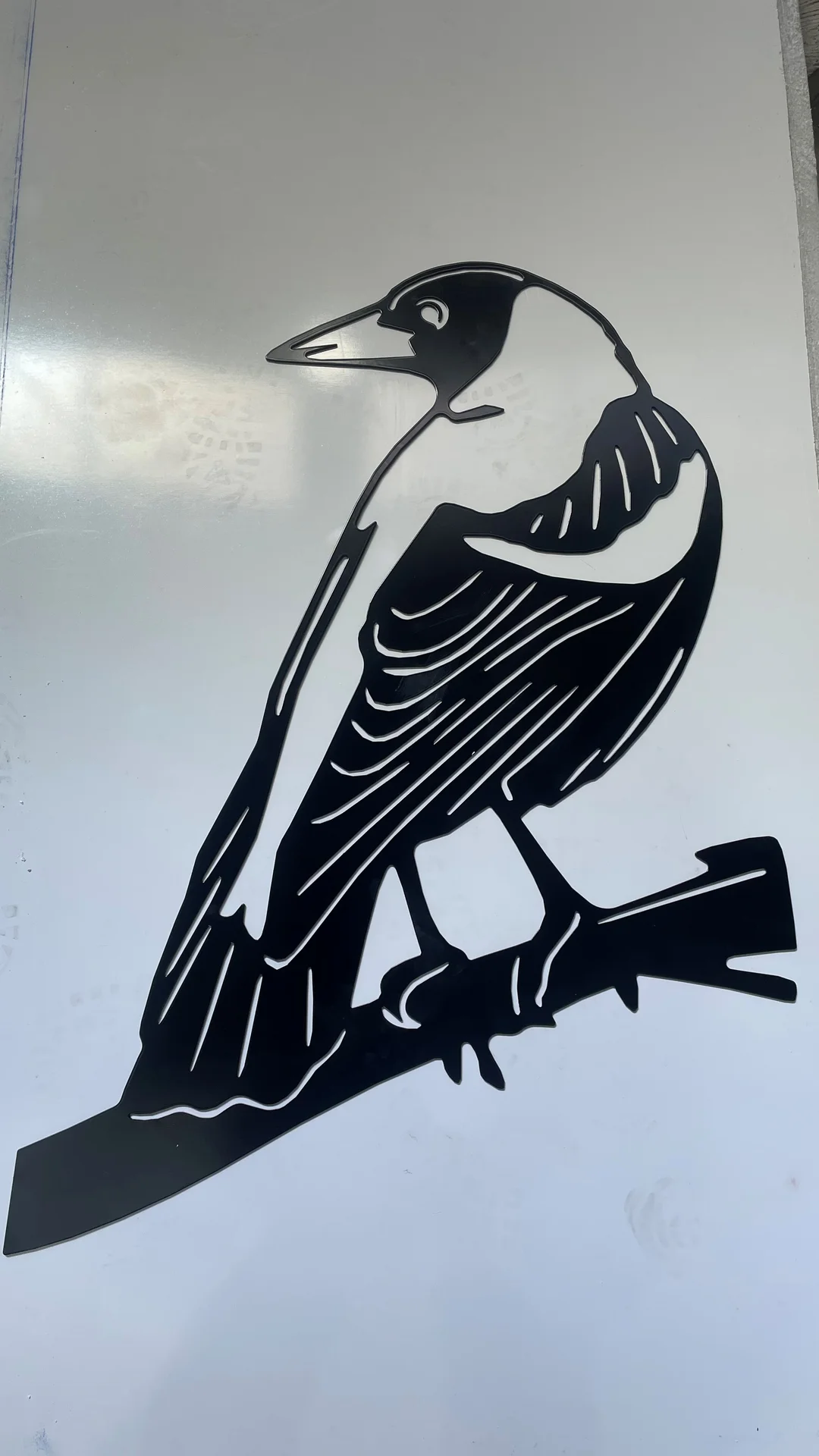 Black laser cut steel magpie on a branch, mounted on a white panel