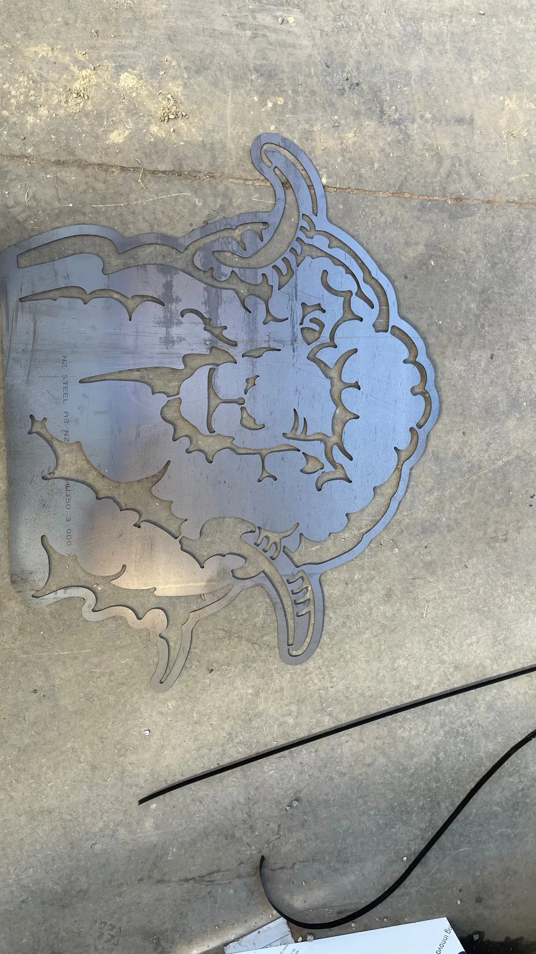 Detailed laser cut steel artwork lying on a concrete workshop floor