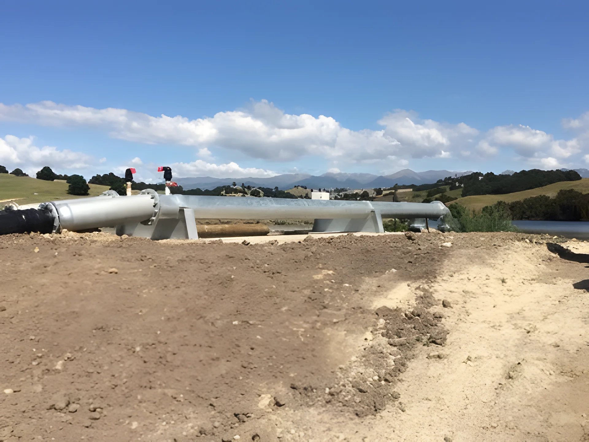 Long run of galvanised pipeline on steel stands over freshly worked ground